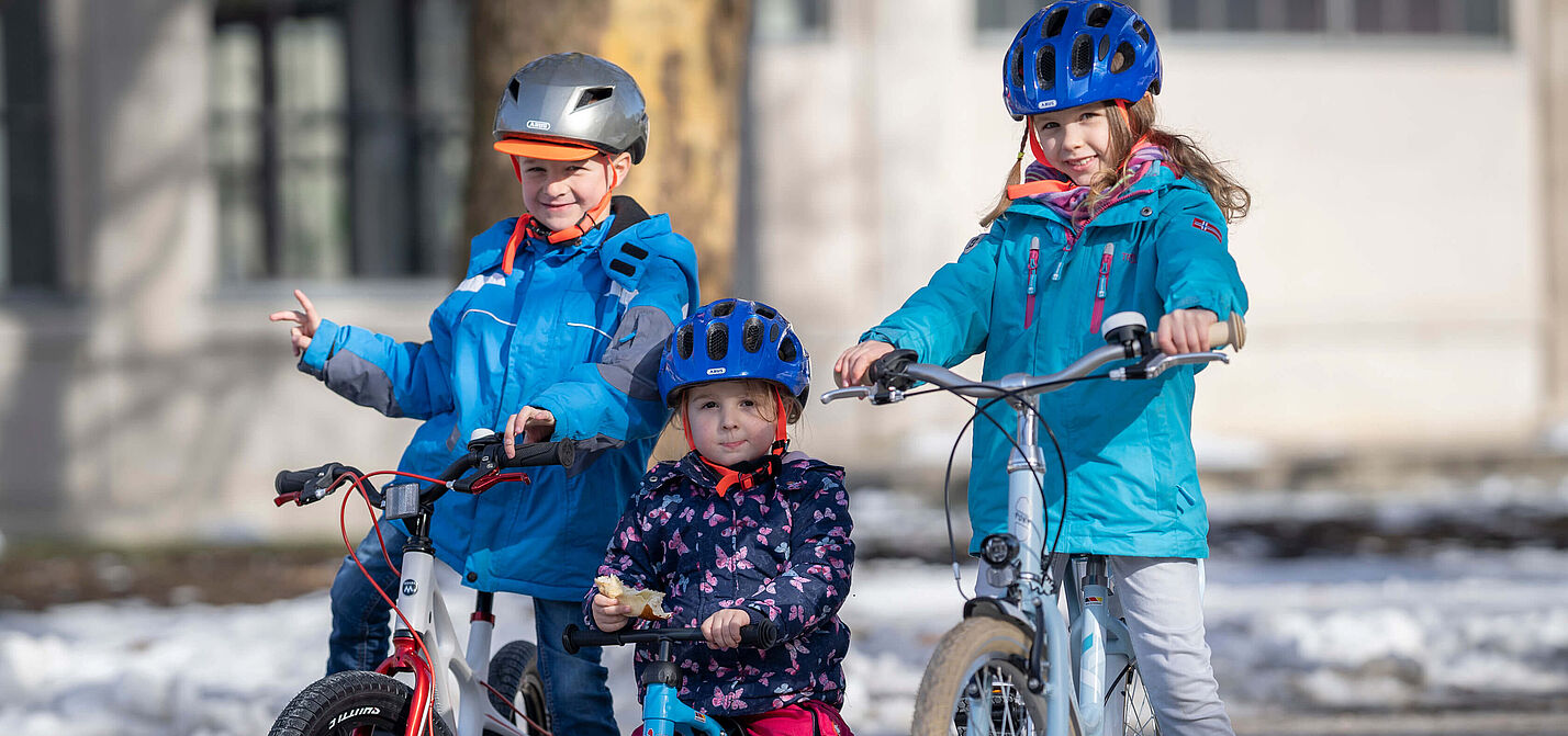 Drei Kinder in unterschiedlichem Alter auf Fahrrädern.